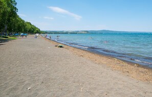 Ein Strand mit sandigem Ufer, einigen Sonnenschirmen und Menschen im Wasser.