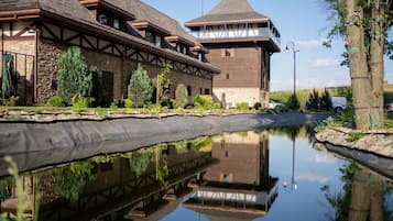 Ein Gebäude mit einer Stein-Fassade, einer Holzterrasse und einem ruhigen Gewässer, das die Struktur spiegelt.