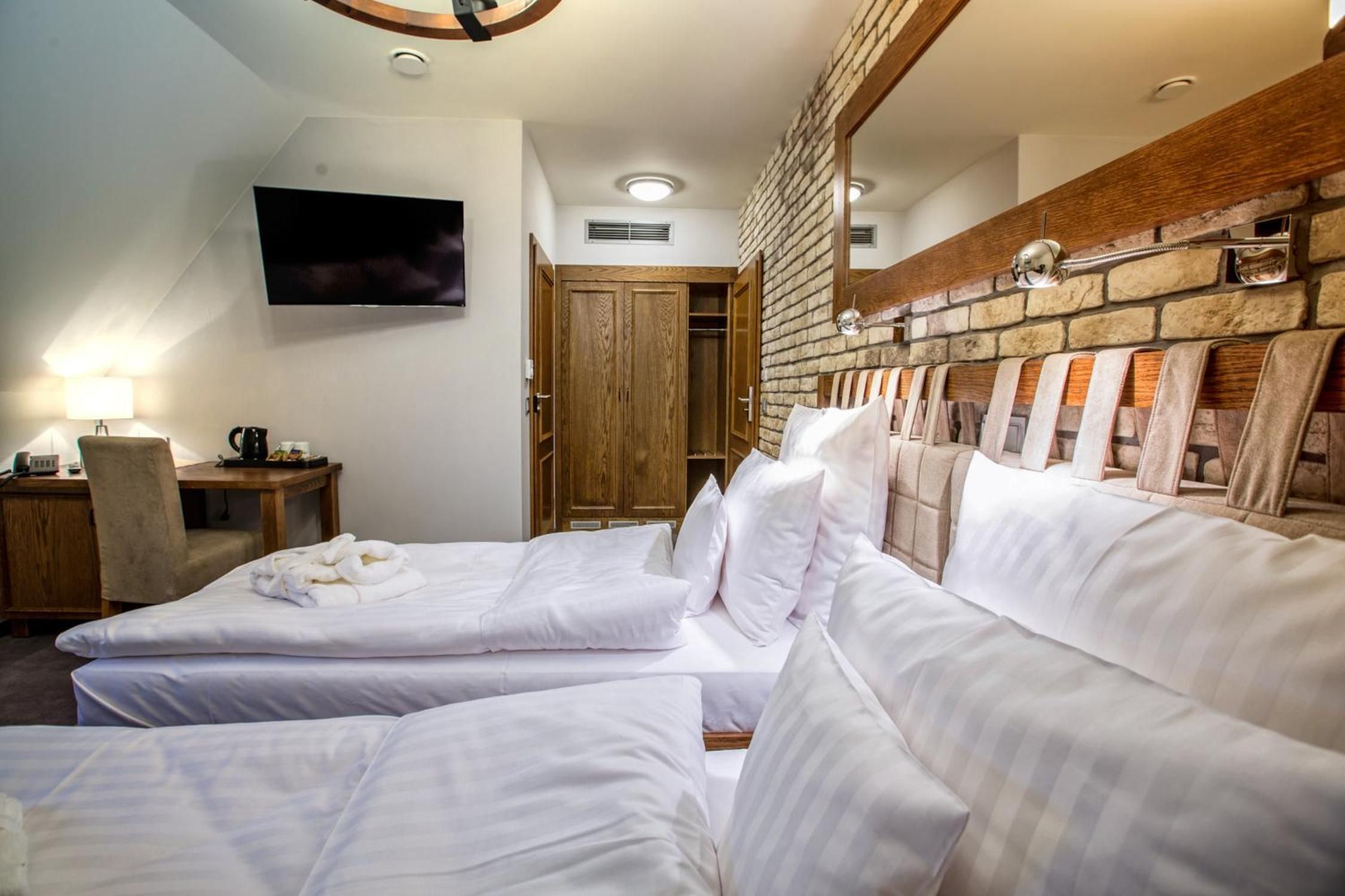 A hotel room with two beds, a TV mounted on the wall, a wooden headboard, and a small table with a lamp.