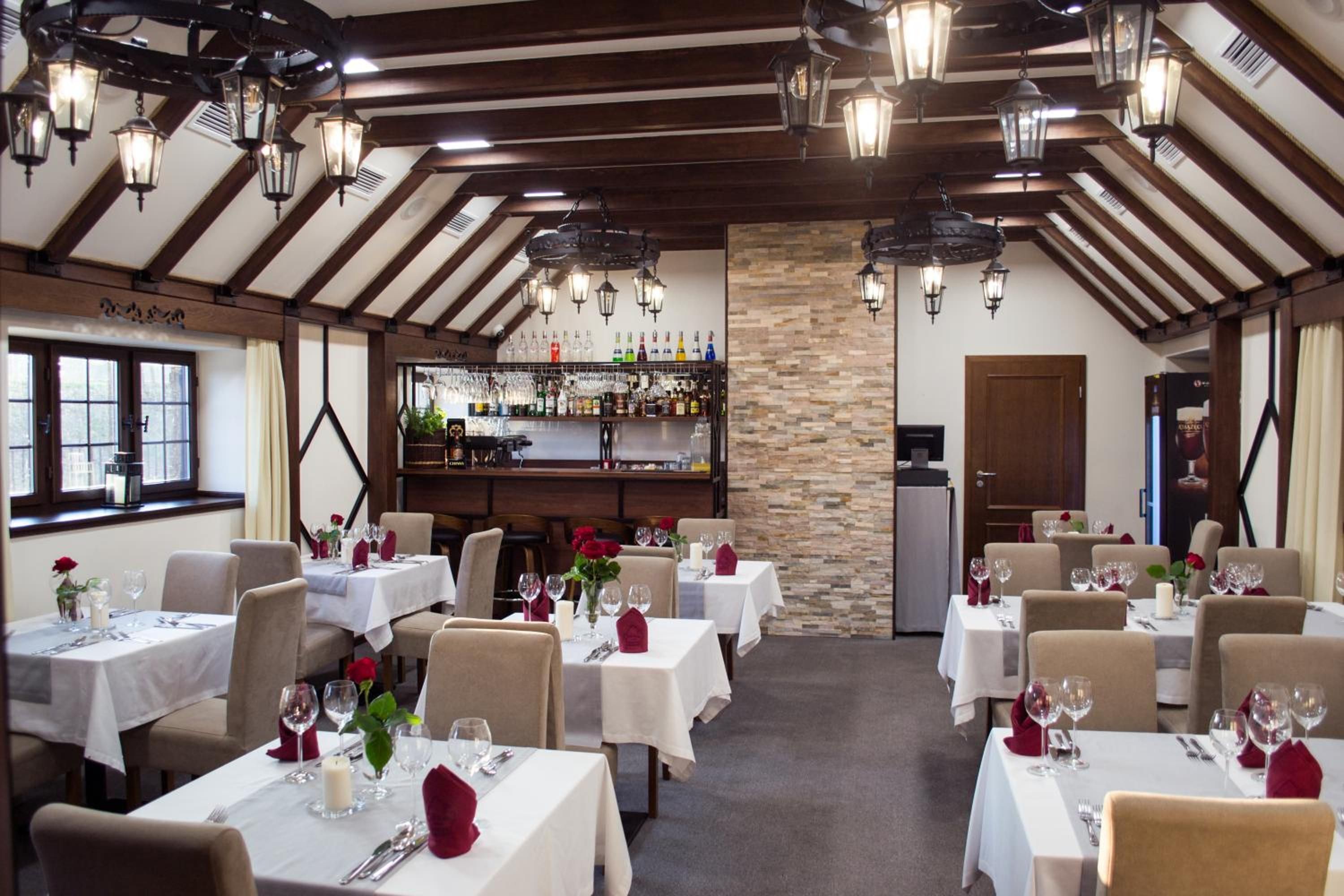 A restaurant with multiple tables set for dining, a bar area with various bottles, and a stone accent wall.