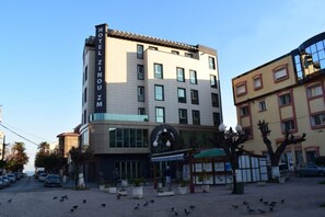 Un hotel con un cartel llamativo, entrada principal y un área pavimentada con plantas en macetas.