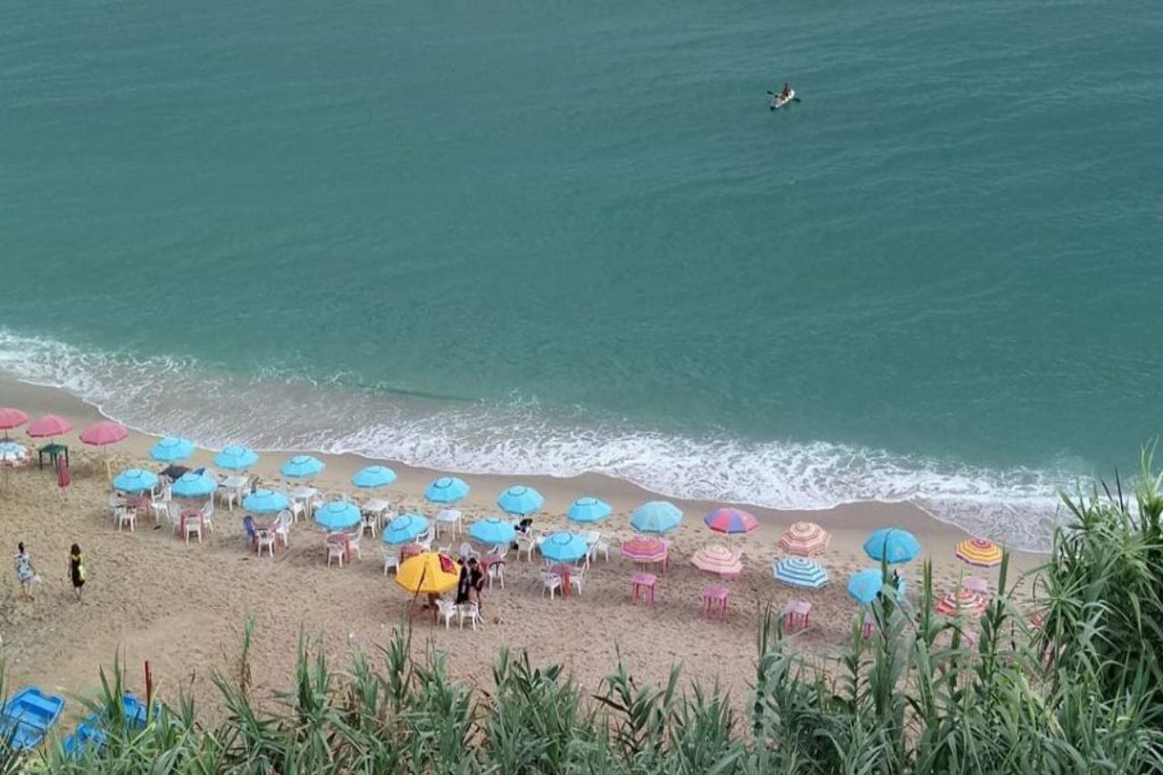 Une plage bordée de rangées de parasols et de chaises, un rivage sablonneux et l’océan.