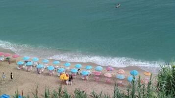 Une plage bordée de rangées de parasols et de chaises, un rivage sablonneux et l’océan.