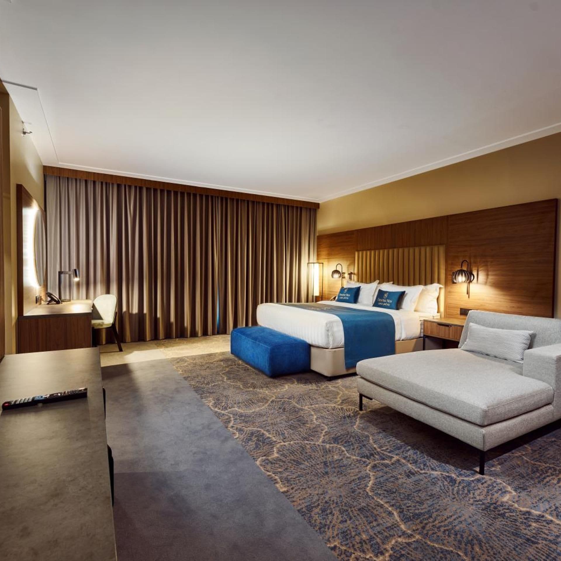 A hotel room with a bed, a sofa, a desk, and a large window with curtains.