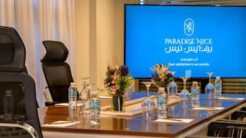A conference room with a large screen displaying 'PARADISE NICE' and a logo, a long table with water bottles, vases with flowers, and black chairs.
