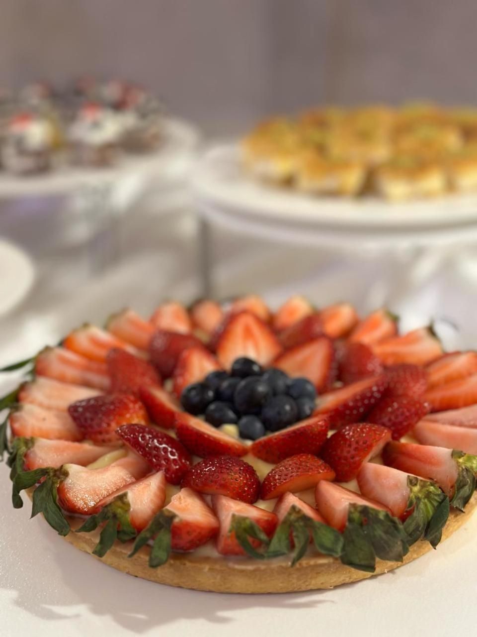 A round fruit tart with strawberries and blueberries on a white plate.