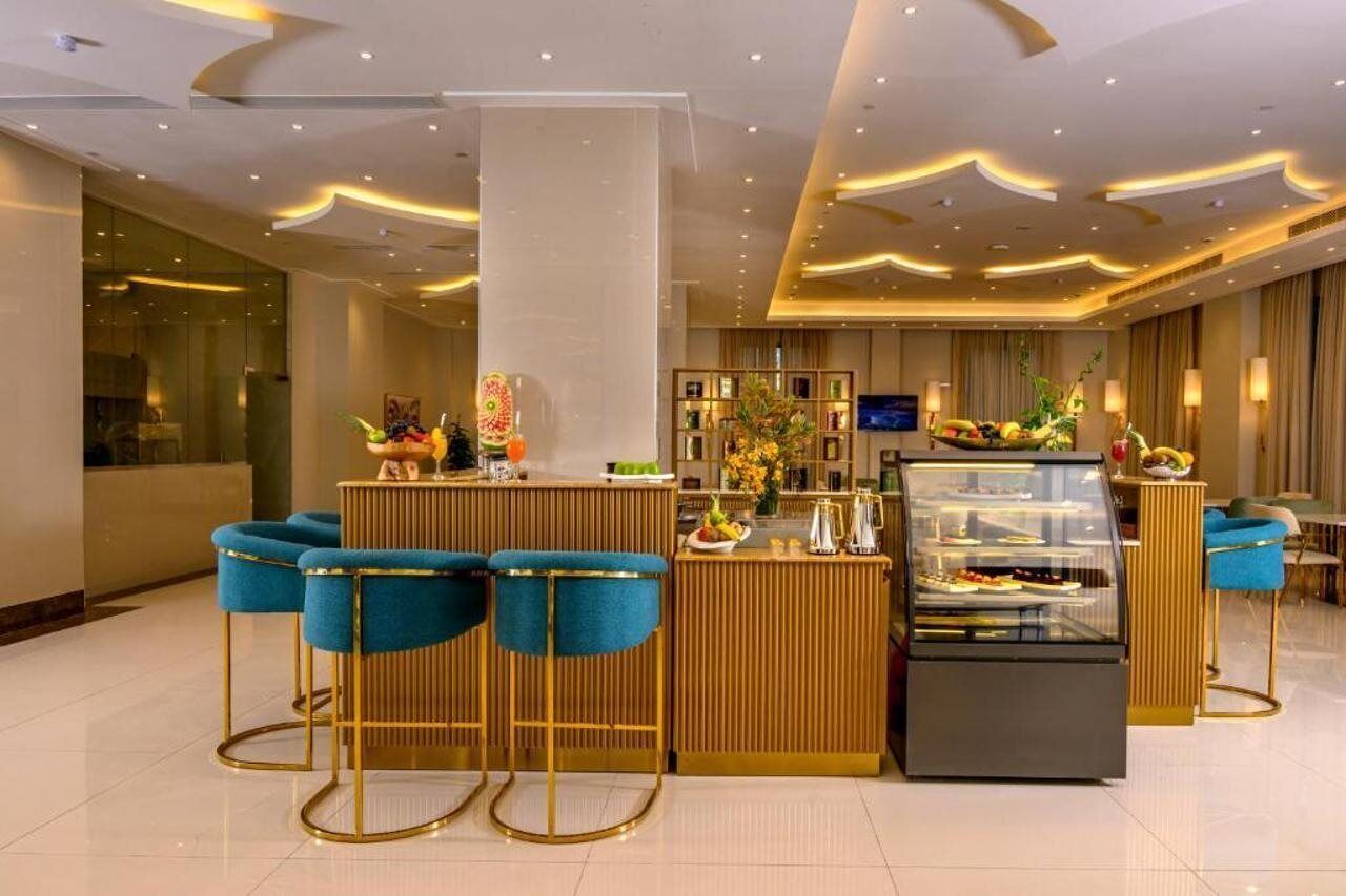 A modern hotel lobby with a reception desk, bar area, and a dessert display.