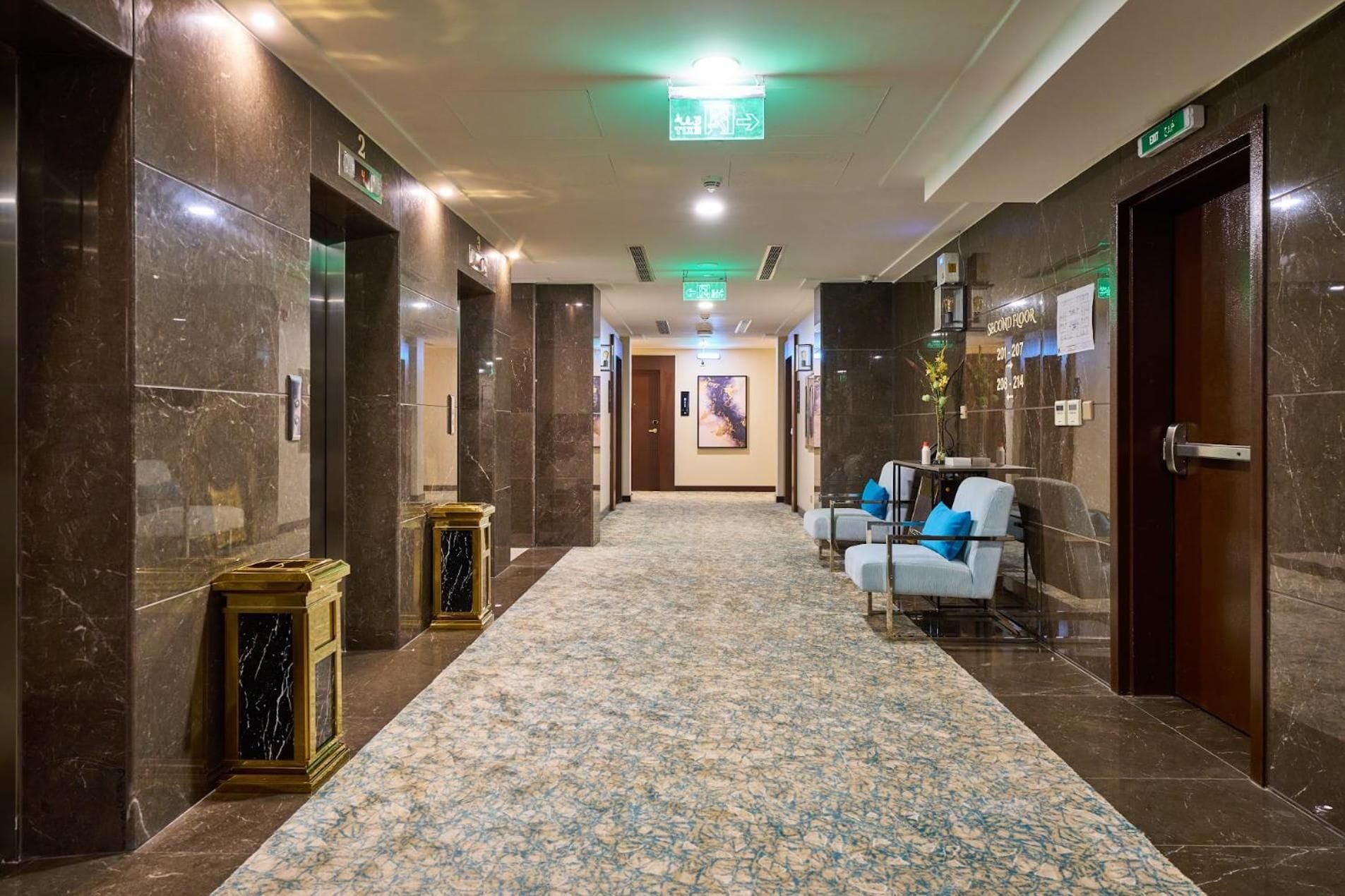 Un vestíbulo de hotel con piso de mármol, zona de recepción y un cartel que indica el segundo piso.