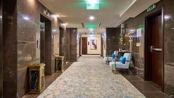 Un vestíbulo de hotel con piso de mármol, zona de recepción y un cartel que indica el segundo piso.