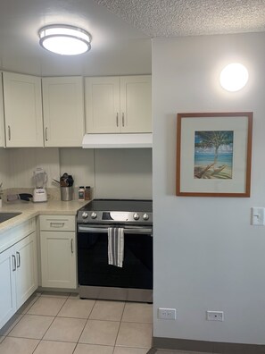 A kitchen with white cabinets, a stove, and a countertop with a blender and other appliances. -  Waikiki apartment, close to the beach, early check in available (Honolulu)