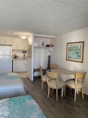 A compact living space with a kitchenette, a dining area with a table and chairs, and a bed with patterned bedding. -  Waikiki apartment, close to the beach, early check in available (Honolulu)