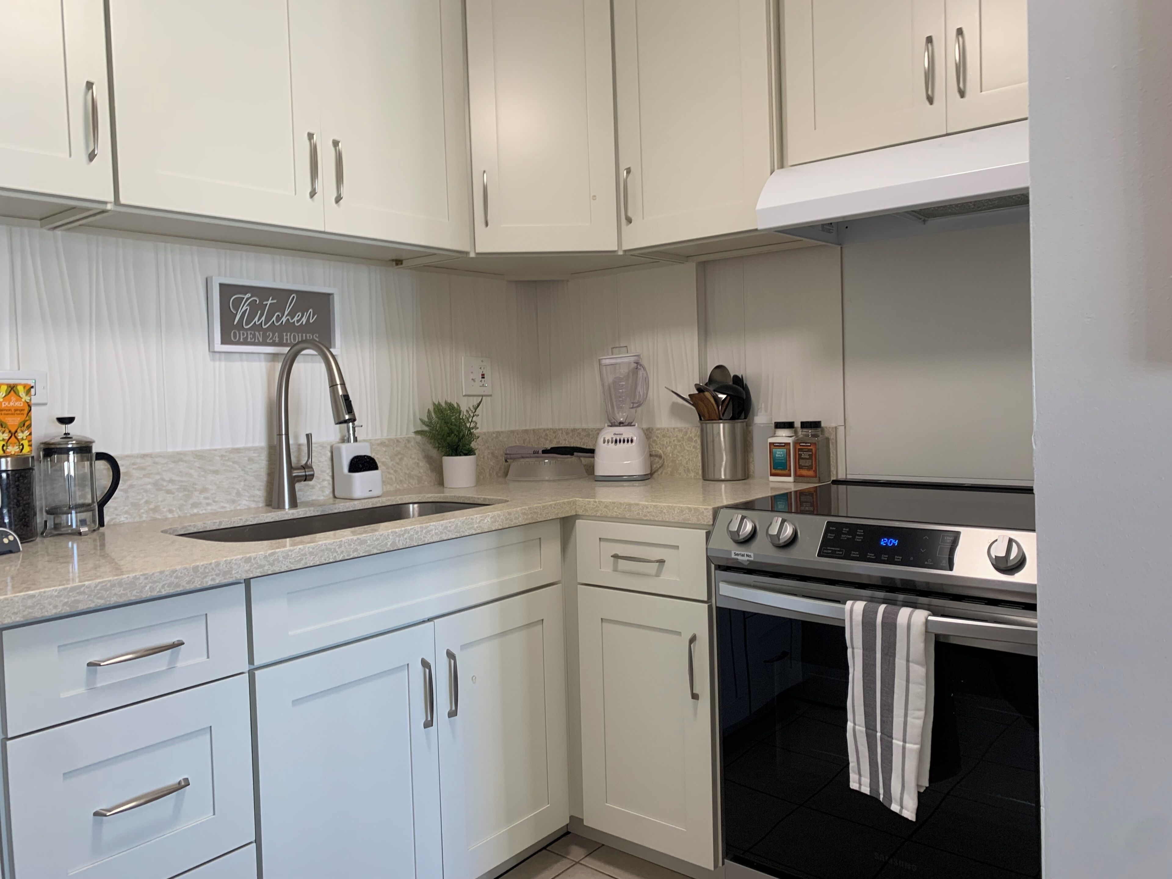 A modern kitchen with white cabinetry, a stainless steel sink, a coffee maker, a blender, and a digital oven.