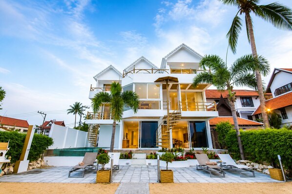 A multi-story residential building with a swimming pool, outdoor seating, and palm trees. - B1 Beachfront (Koh Samui)