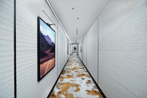 A hallway with a patterned carpet, framed artwork on the walls, and a ceiling with recessed lighting.