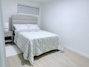 A bedroom with a bed, nightstand, and a window with blinds. - Cozy 2BR Basement Suite Rosenthal Stay by WEM (Edmonton)