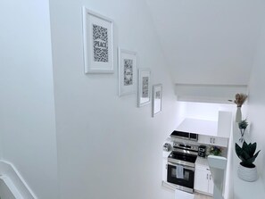 A modern kitchen with white cabinetry and stainless steel appliances, including a stove and oven. There are three framed artworks on the wall, and a potted plant is visible on the right side. - Cozy 2BR Basement Suite Rosenthal Stay by WEM (Edmonton)
