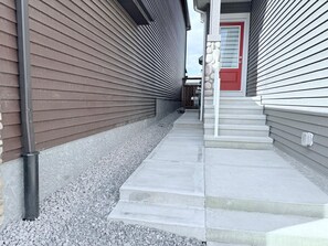 A narrow pathway leading to a red door, flanked by two buildings with siding. - Cozy 2BR Basement Suite Rosenthal Stay by WEM (Edmonton)