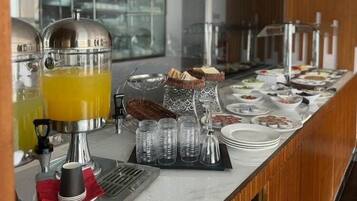 Een buffetopstelling met een sapdispenser, een broodmand en diverse gerechten.
