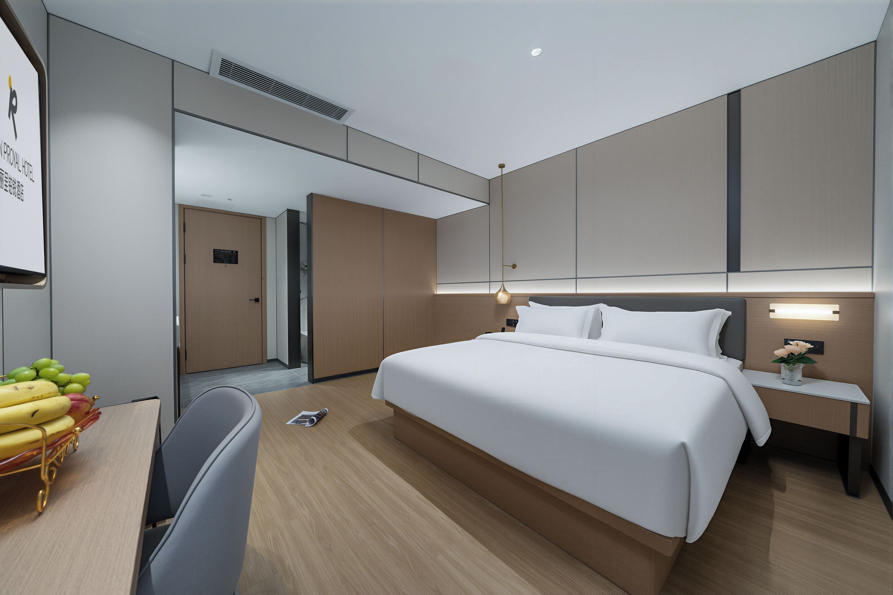 A modern hotel room with a large bed, bedside table, and a desk with a chair.
