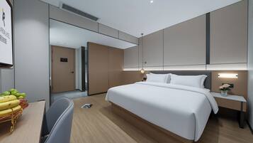 A modern hotel room with a large bed, bedside table, and a desk with a chair.