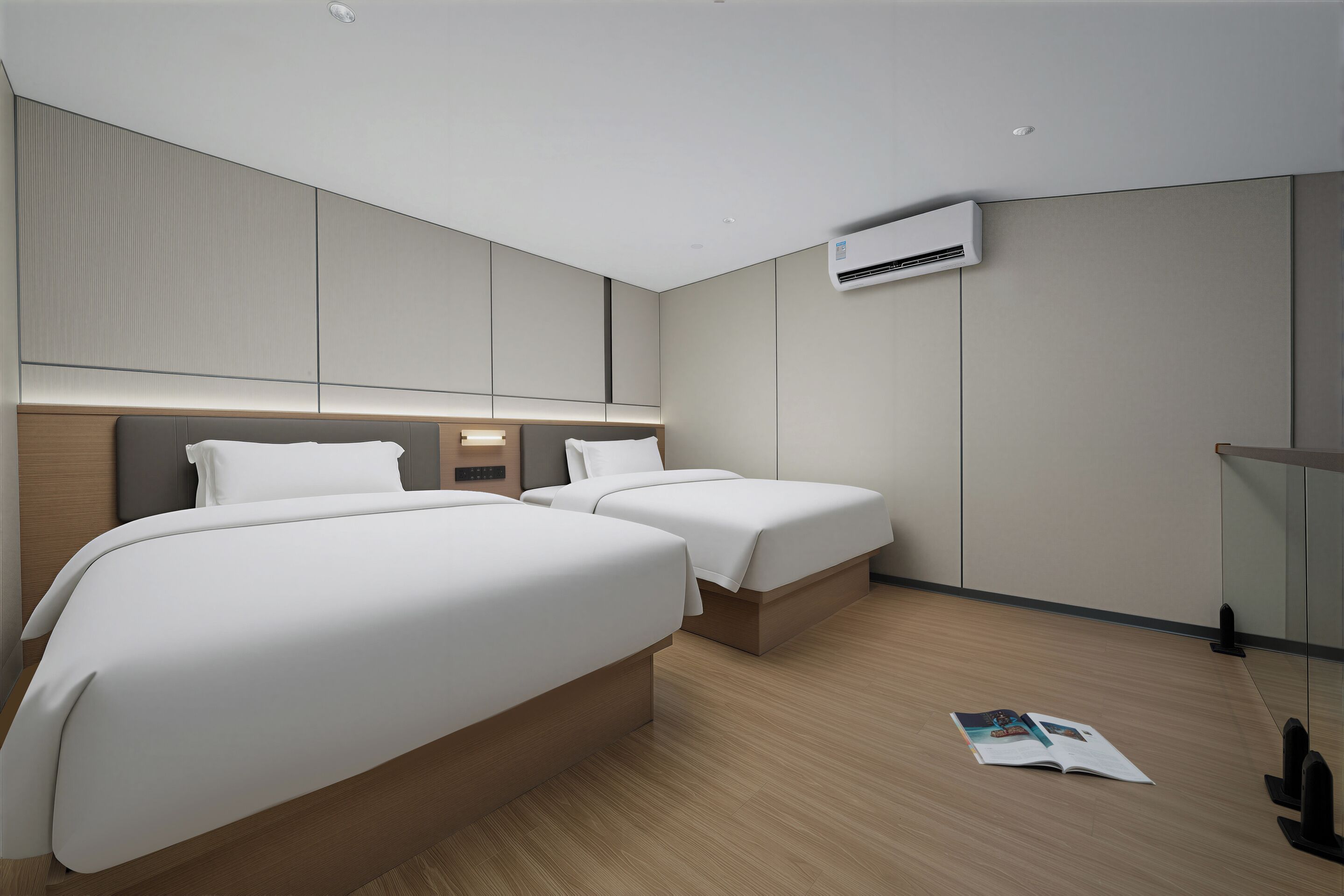 Habitació d'hotel moderna amb dos llits, una taula de treball integrada, aire condicionat fixat a la paret i una revista a terra.