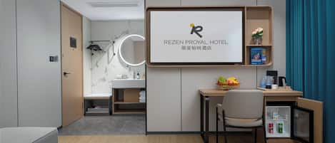 Habitación de hotel con cama, escritorio, silla, minibar y una pantalla grande que muestra el nombre del hotel.