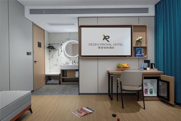 A hotel room with a bed, a desk, a chair, a minibar, and a large screen displaying the hotel name. - Rezen Proyal Hotel Ezhangtan Branch (Guangzhou)