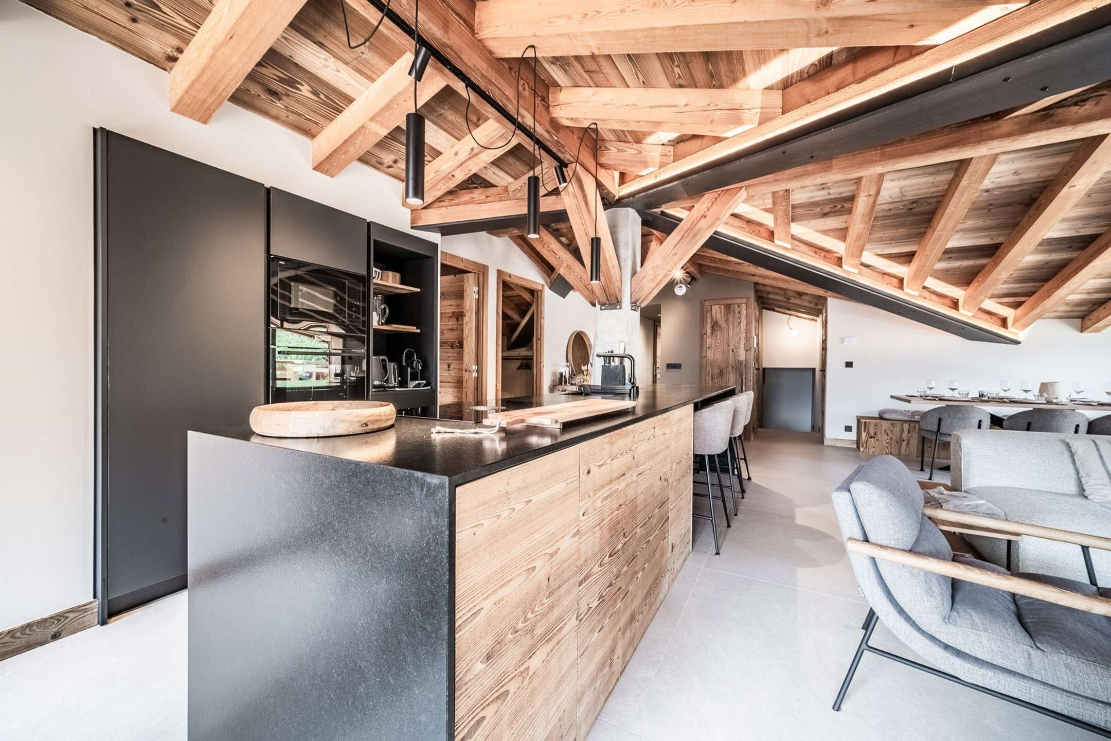 Una cocina moderna con techo de madera, encimera negra y barra con taburetes.