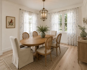 Un comedor con una mesa de madera, seis sillas, un jarrón con plantas y una lámpara colgante.