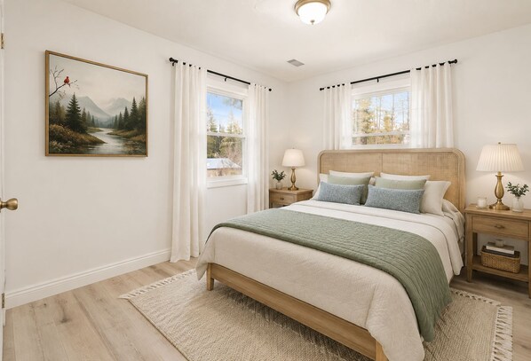 Un dormitorio con cama, mesitas de noche, lámpara, un cuadro y vistas al exterior.