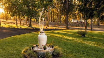 Un parc avec une fontaine centrale, entourée de pelouses et d’arbres.