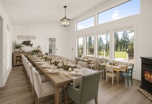 Un comedor amplio con una larga mesa lista para una comida, ventanas grandes y una chimenea.
