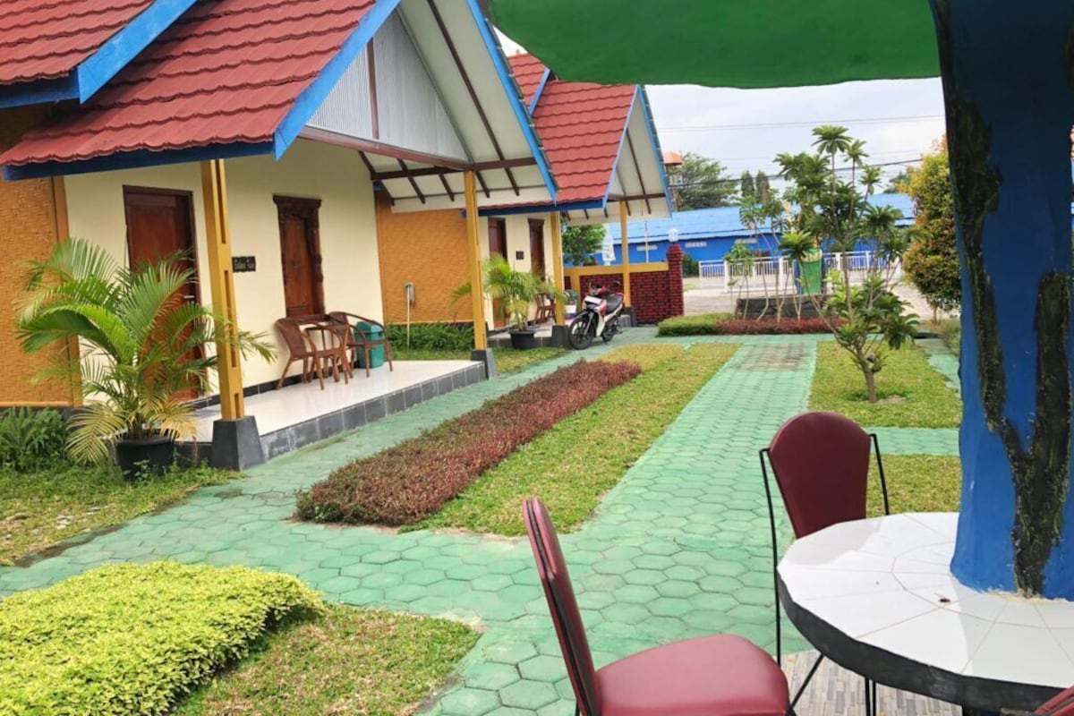 A courtyard with a paved walkway, outdoor seating, and a building with a red roof.
