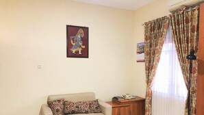A living room with a sofa, a small cabinet, a framed picture on the wall, and a window with curtains. - Hotel Galuh and Water Park Prambanan  (Prambanan)