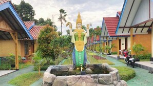 A statue in a courtyard with a stone fountain, surrounded by buildings with red roofs and a paved walkway. - Hotel Galuh and Water Park Prambanan  (Prambanan)