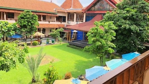 A courtyard with a stage, a blue umbrella, and a building with a red roof. - Hotel Galuh and Water Park Prambanan  (Prambanan)