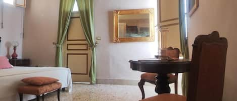 Habitación de hotel con cama, escritorio, silla, espejo y ventana con cortinas verdes.