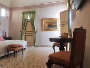 A hotel room with a bed, a desk, a chair, a mirror, and a window with green curtains. - Roccamelia Experience (Mazara del Vallo)