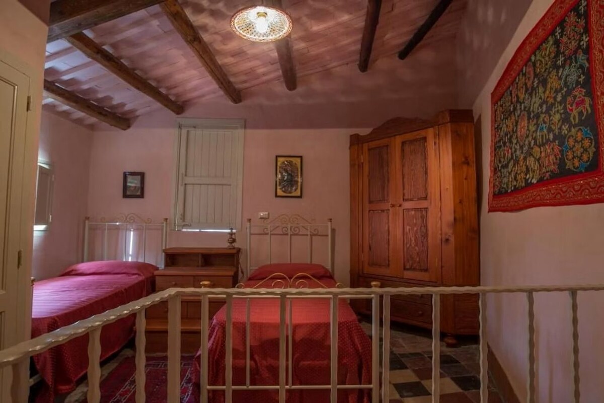 A room with two beds, a wooden wardrobe, a door, and a patterned tapestry on the wall.