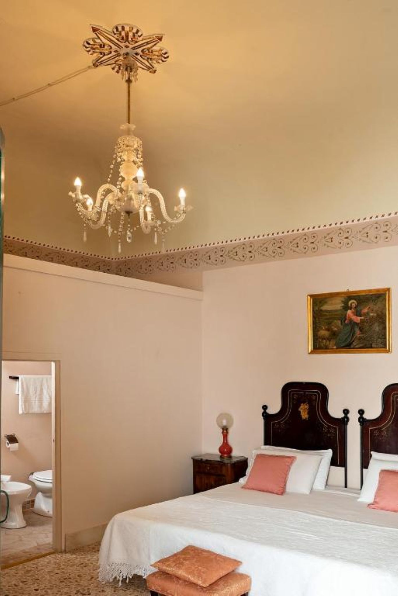 Une chambre à coucher avec un grand lit, un lustre, un tableau au mur et une salle de bain visible au fond.