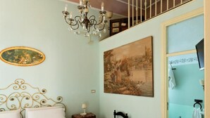 A bedroom with a bed, a chandelier, a painting, and a window. - Roccamelia Experience (Mazara del Vallo)