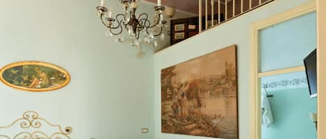 A bedroom with a bed, a chandelier, a painting, and a window.