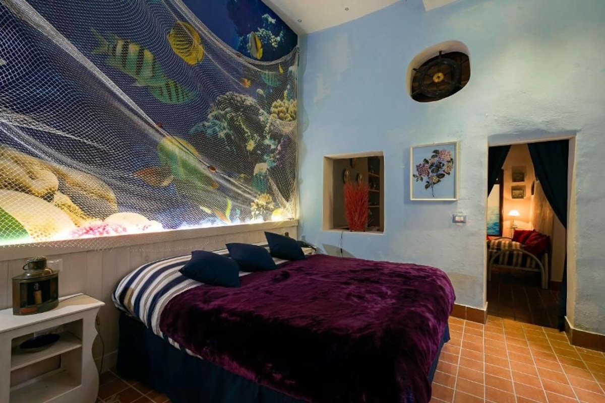 A bedroom with a bed, a wall mural, a small window, and a door leading to another room.