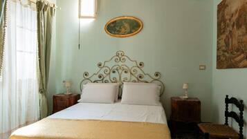A bedroom with a bed, two bedside tables, a chair, a painting on the wall, and a window with curtains.