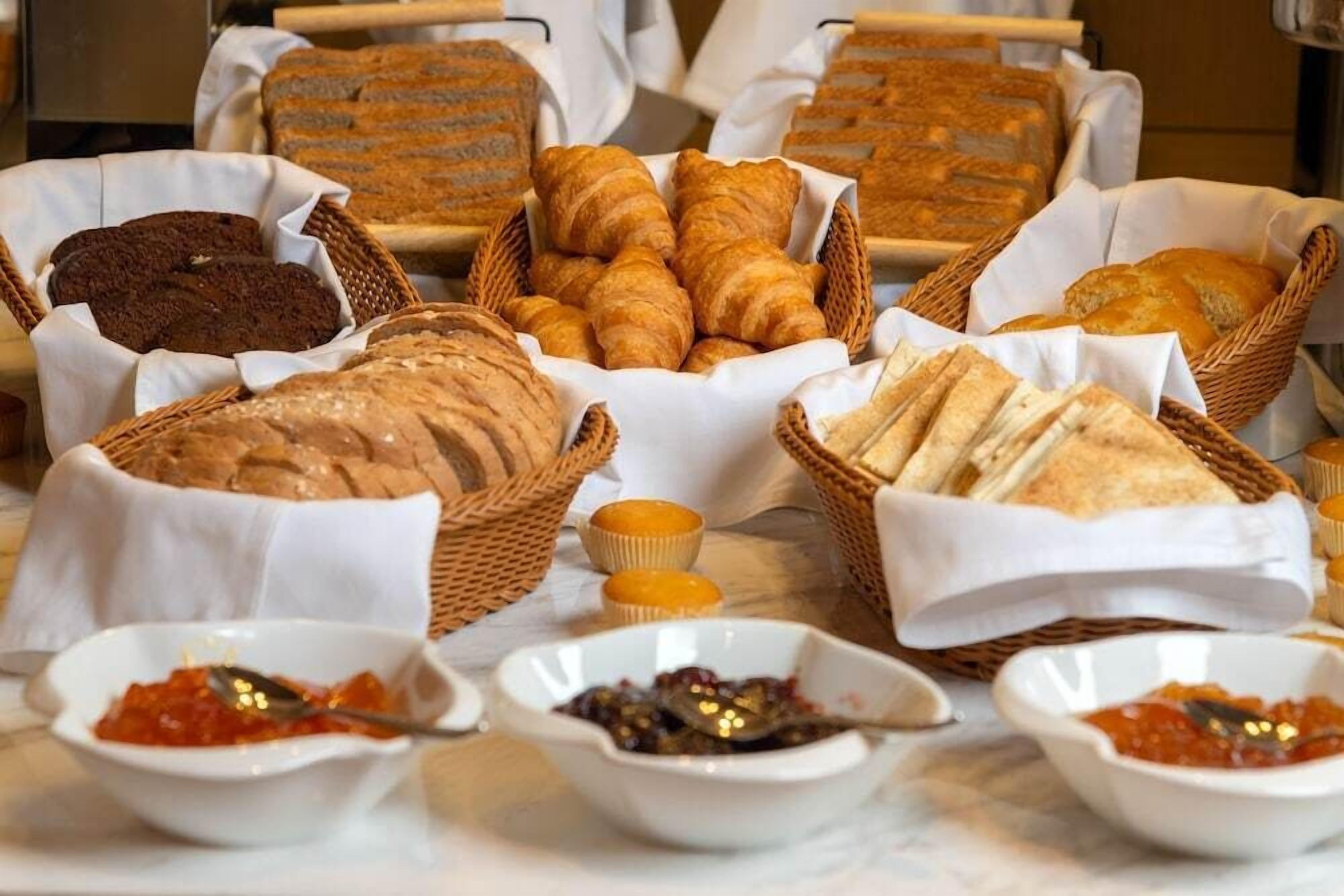 A variety of baked goods including bread, croissants, and muffins, along with small bowls of spreads.