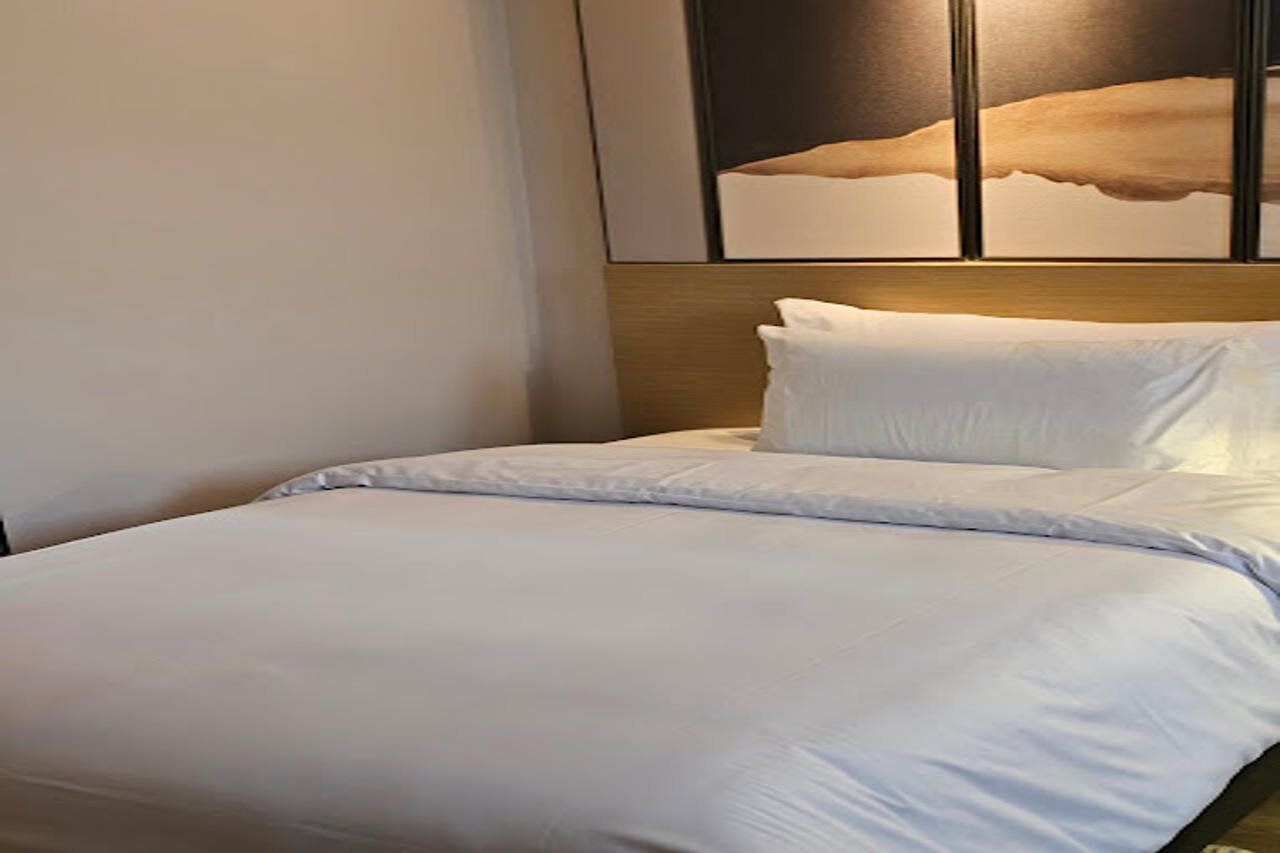 Une chambre d’hôtel avec un lit, une tête de lit et une œuvre d’art accrochée au mur.