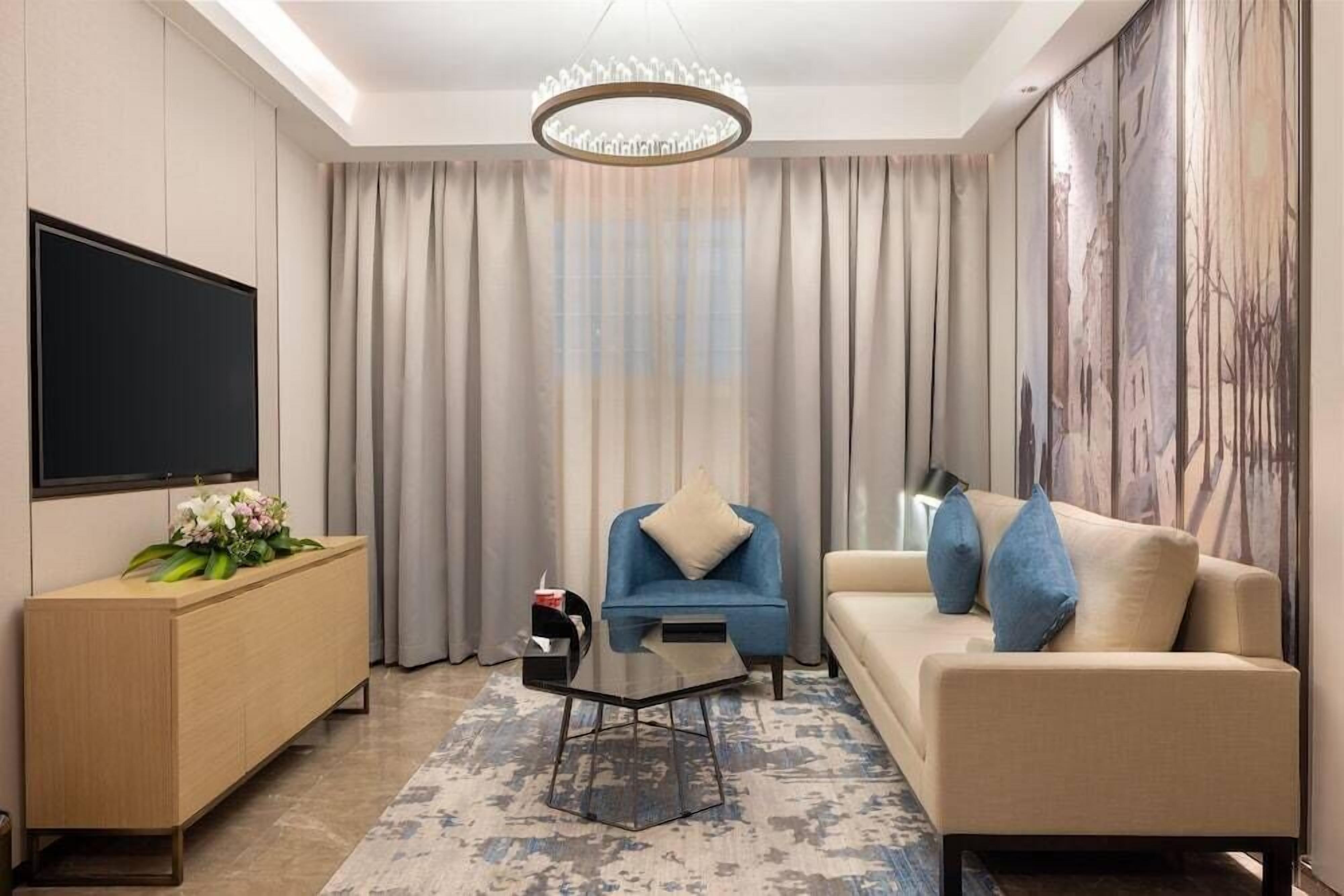 A modern living room with a flat-screen TV, a blue armchair, a beige sofa, and a coffee table.