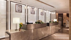 Una recepción con mostrador de mármol, retratos enmarcados y un jarrón con flores.
