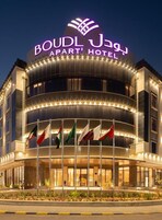 El exterior del Apart Hotel Boudl Jag, con un cartel llamativo, varias banderas y una entrada bien iluminada.