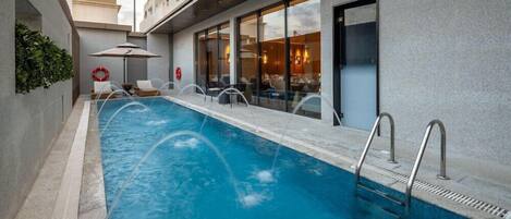 A swimming pool with lounge chairs and a sun umbrella, adjacent to a building with large windows and a door.